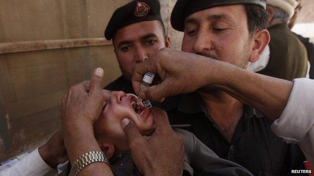 Polio workers give polio vaccine drops to a child as police stand guard during a vaccination campaign in Peshawar, the capital of Khyber-Pakhtunkhwa province March 30, 2014