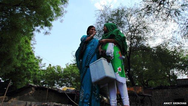 Two women talking, one with a large ice box