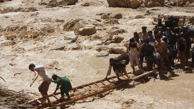 Travellers use a ladder to cross a river where rains have washed away the main Mazar-Kabul highway