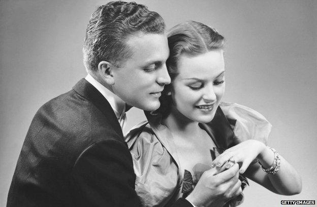 Historical image of a newly engaged couple looking at ring on woman's finger