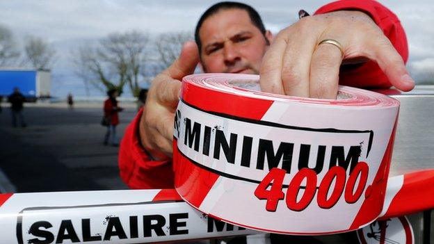 A member of the Swiss UNIA workers union sets a ribbon around a petrol pump during a protest at a filling station