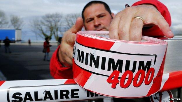 A member of the Swiss UNIA workers union sets a ribbon around a petrol pump during a protest at a filling station