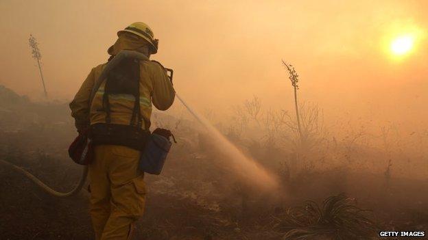 A firefighter puts down hot spots in front of a house in the hills in San Marcos, California, 1 May 2014