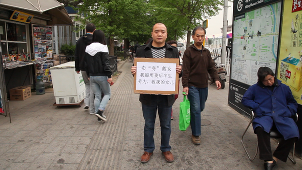 Cheng Bangjian stands in a Beijing street and holds a sign which reads: "I will work the rest of my life for anyone who funds my daughter's medical care."