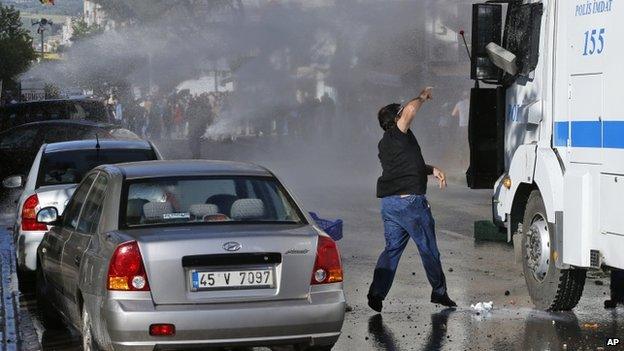 An anti-government protester throws a stone at a police water canon as it is used against protesters during clashes with police in Soma