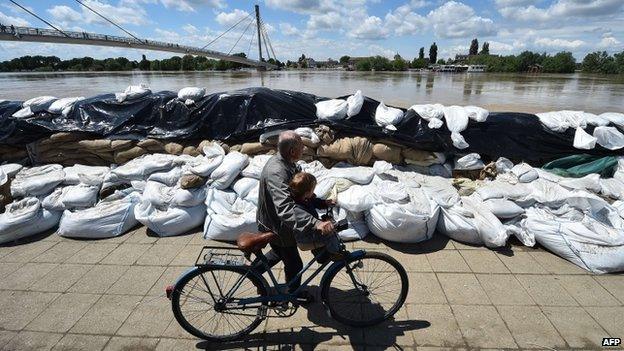 A man pushes a bicycle past sand bags protecting the banks of the Sava river in Sremska Mitrovica on 18 May 2014