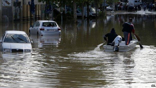 People paddle a boat down a flooded street in Obrenovac, some 30km (18 miles) south-west of Belgrade