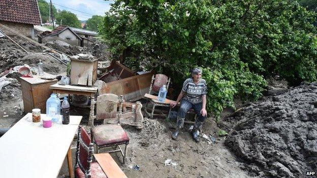 A woman sits on a chair as she rests next to furniture in her mud covered back yard in Krupanj