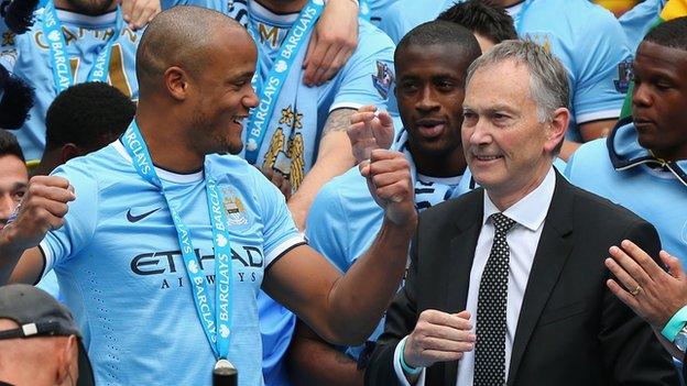 Premier League Cheif Executive Richard Scudamore looks on as Vincent Kompany of Manchester City celebrates with his team-mates.