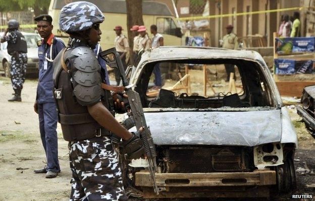 A policeman stands near damaged vehicles in Sabon Gari, Kano, Nigeria on 19 May 2014