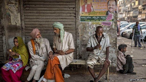 Indians drink tea under a poster showing Narendra Modi at a chai stall on May 21, 2014 in Delhi