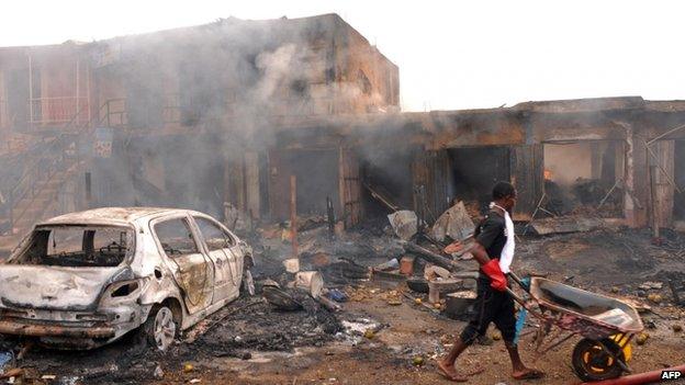 A boy pushes a wheelbarrow past the wreckage of a burnt vehicle and burning shops following a bomb blast at Terminus market in the central city of Jos on 20 May 2014 - an attack the authorities suspect was perpetrated by Boko Haram