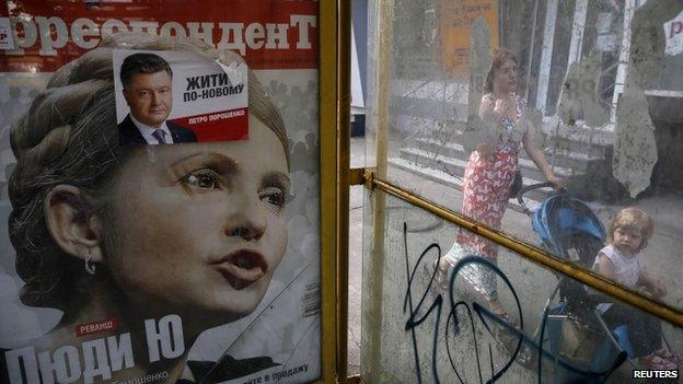 A woman pushes her child on a pram past an advertisement of a magazine cover of former prime minister and presidential candidate Yulia Tymoshenko and an election poster for businessman, politician and presidential candidate Petro Poroshenko, a day after Ukrainian presidential elections, in Kiev May 26, 2014.