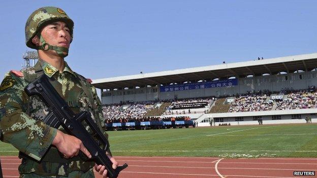 A paramilitary policeman stands guard near trucks carrying criminals and suspects during a mass sentencing rally at a stadium in Yili, Xinjiang Uighur Autonomous Region, 27 May 2014