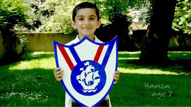 A seven year old boy holding up a large cut out of the Blue Peter Sport badge