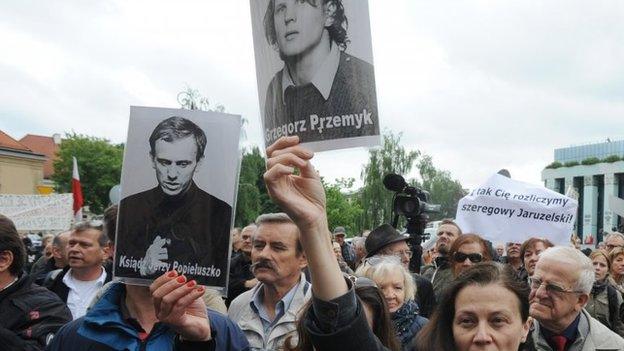 Protesters holding photos of victims of the communist regime, in front of the Warsaw cathedral