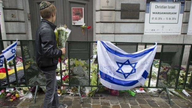 A Jewish boy stands with flowers in front of an Israeli flag and flowers laid in front of the Jewish Museum in Brussels on 26 May 2014