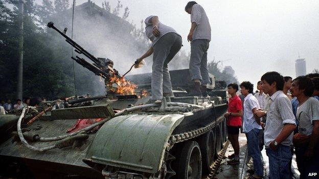 This archived photo shows Chinese residents checking an armoured personnel carrier which was set on fire by rioters on 4 June, 1989 near Tiananmen Square in Beijing