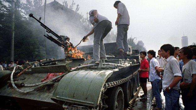 This archived photo shows Chinese residents checking an armoured personnel carrier which was set on fire by rioters on 4 June, 1989 near Tiananmen Square in Beijing