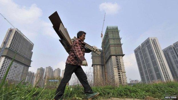 A garbage collector walks past residential and office buildings in construction, in Hefei, Anhui province, in this 3 April 2014 file photo