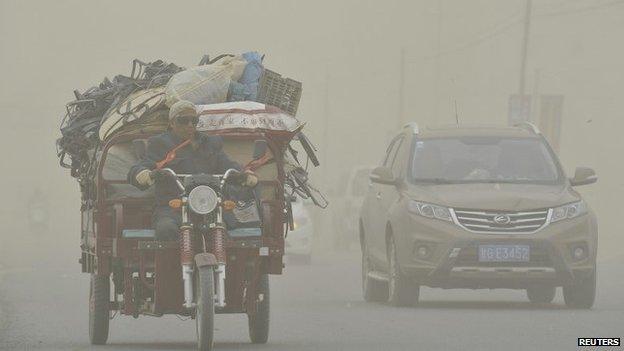 A motorcyclist rides past a car during a dust storm in Hami, Xinjiang Uygur Autonomous Region, 23 April 2014