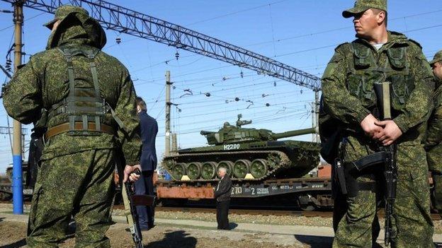 Armed Russian servicemen stand guard as Russian tanks arrive at a train station in the Crimean settlement of Gvardeiskoye