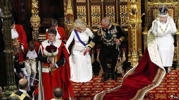 The Prince of Wales and the Duchess of Cornwall reach towards a pageboy who fainted as Queen Elizabeth II delivers her speech