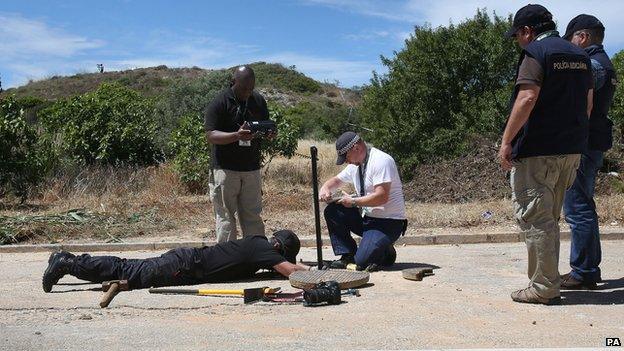 Police look remove a manhole cover on the edge of the 12-acre search site in Praia da Luz