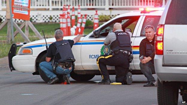 Police officers take cover behind their vehicles in Moncton, New Brunswick, on 4 June 2014