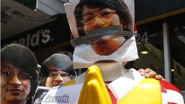 Thai protesters wear masks of Sombat Boonngamanong, next to a statue of Ronald McDonald during a rally at a shopping district in central Bangkok on 25 May, 2014