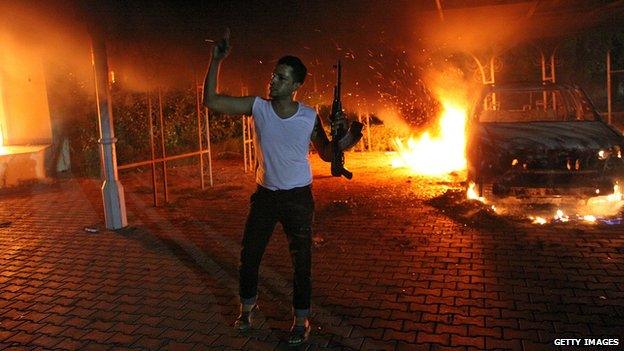 A militant brandishing a gun poses in front of a burning vehicle inside the US consulate compound in Benghazi, Libya late on September 11, 2012