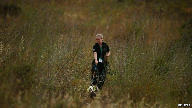 A police officer and a sniffer dog search scrubland