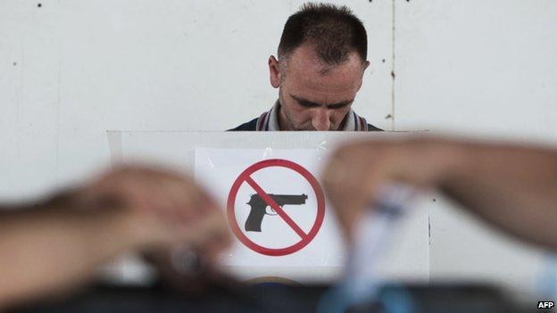 A Kosovo Albanian man prepares his ballot at a polling booth with a "no guns" sign before voting at a polling station in Pristina on June 8,