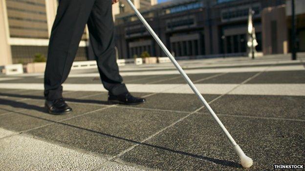 Blind person with stick walking across square