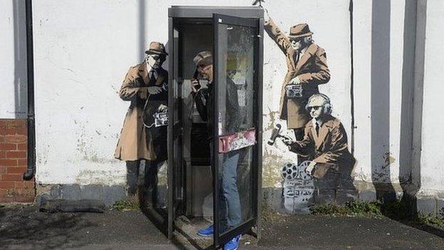 Man in phonebox with artwork on wall behind