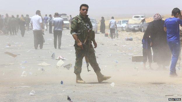 A member of Kurdish security forces stands guard as families fleeing violence in the Iraqi city of Mosul wait at a checkpoint on the outskirts of Irbil, in Iraq's Kurdistan region on 10 June 2014.