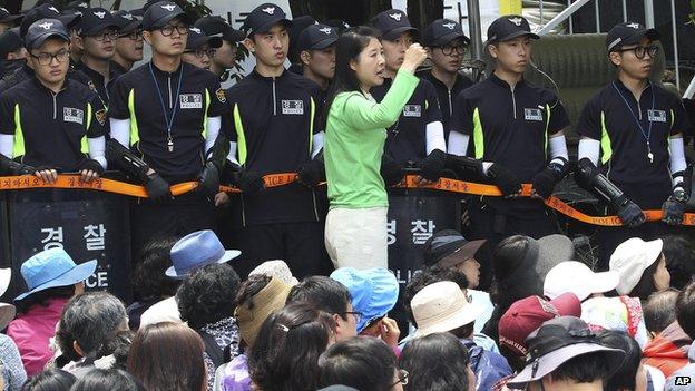 An Evangelical Baptist Church believer shouts slogans against the government as police officers stand guard in font of believers sitting by the main gate of the church in Anseong, South Korea, on Wednesday, 11 June 2014