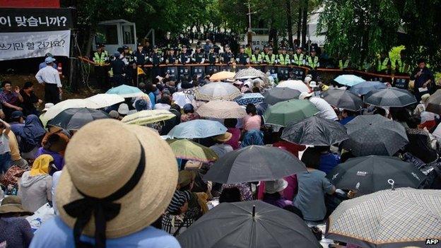 Followers sit before a line of police outside the compound of Yoo Byung-Eun, in Anseong on June 11