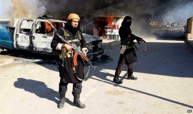 Undated image posted on a militant website in January 2014 shows Islamic State of Iraq and the Levant fighters next to a burning vehicle in Iraq's Anbar Province