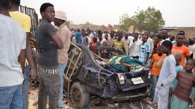 People look at the wreckage of a car on 2 March 2014, after two deadly explosions in a crowded neighbourhood of Maiduguri, Nigeria