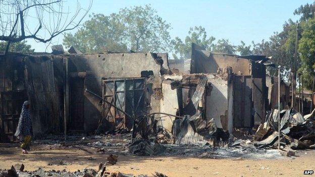 A woman walks past burnt houses after an attack by scores of Islamist militants on 20 February 2014 in the north-east Nigerian town of Bama