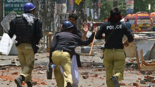 A follower of preacher Tahirul Qadri (background centre) reacts while beaten by Pakistani policemen during clashes in Lahore on June 17, 2014.