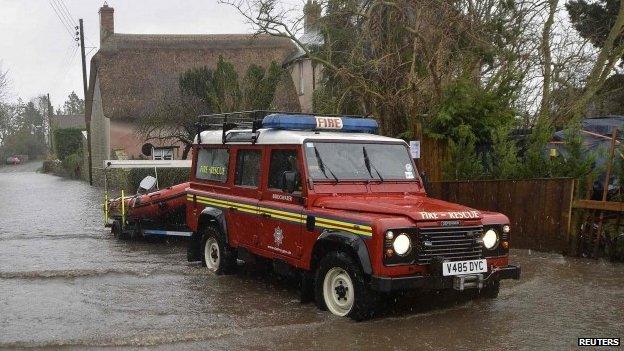 An emergency services vehicle pulls a boat through flood waters in the village of Thorney