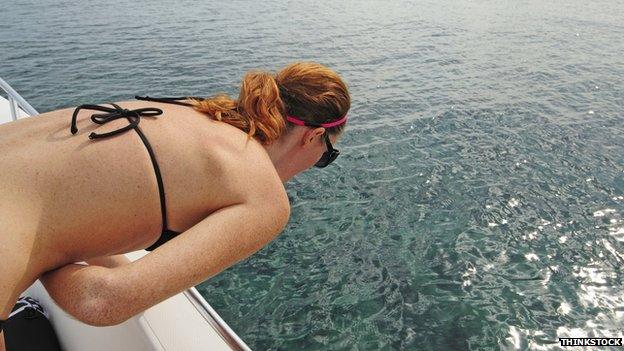 Woman leaning over the side of a boat to be sick