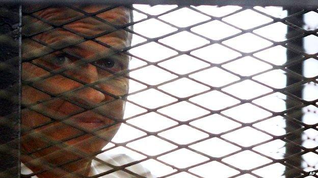 Al-Jazeera journalist Peter Greste looks out from a cage in a courtroom in Cairo, Egypt - Monday 23 June 2014