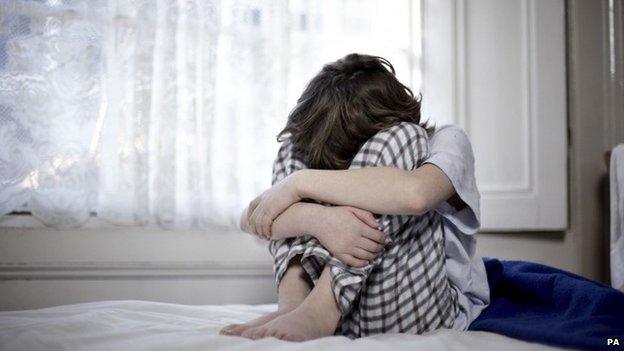 A child sat on a bed with his head in his hands