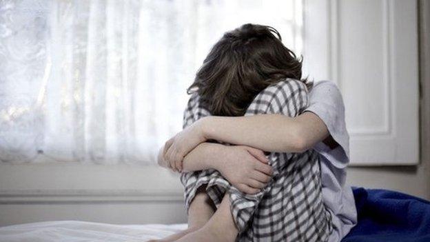 A child sat on a bed with his head in his hands