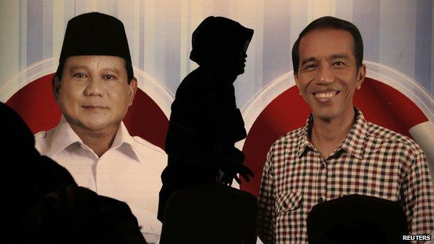 A woman walks past a poster of Indonesia's presidential candidates Prabowo Subianto and Joko Widodo during a debate in Jakarta on 15 June, 2014