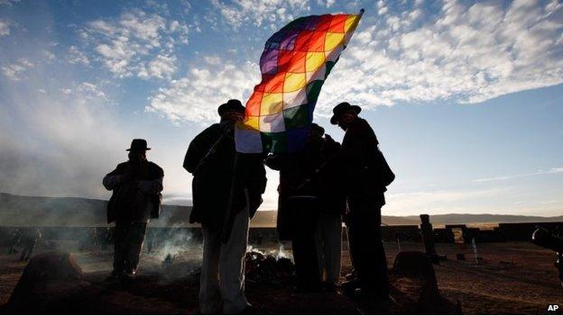 Aymara indigenous men with a Wiphala flag attend a new years ritual at the ruins of the ancient civilization of Tiwanaku located in the highlands in Tiwanaku, Bolivia, early Saturday, June 21, 2014