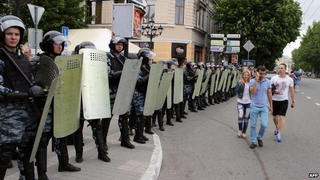 People walk past officers the Russian riot police force OMON blocking a street in the Crimean capital Simferopol